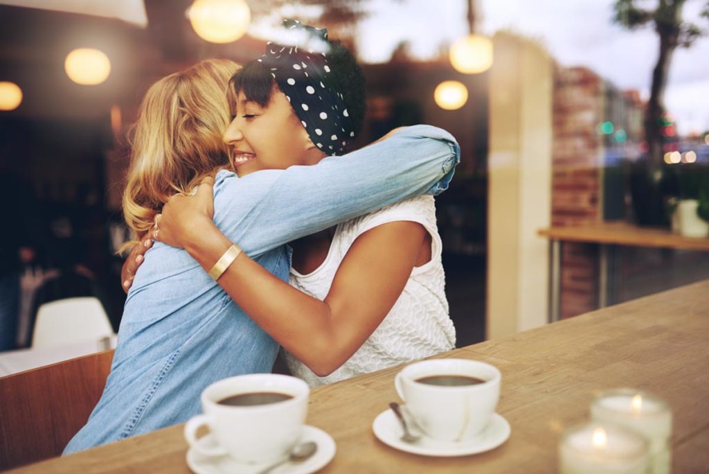 image of two friends hugging at a coffee shop while having coffee as a solution to what to get someone for their sober anniversary