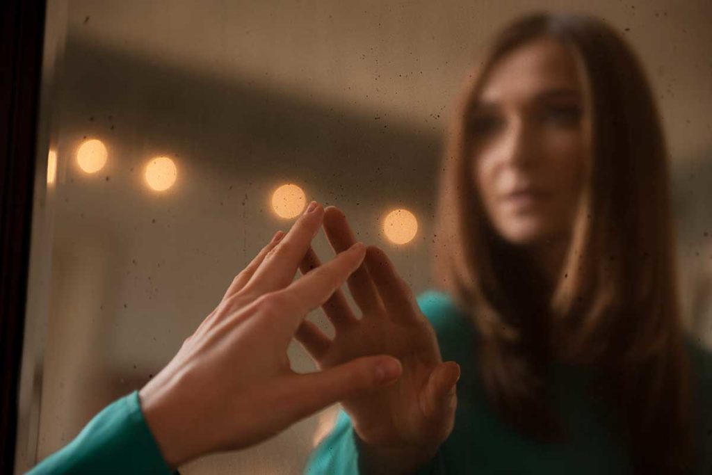 woman reaching out to touch her reflection in a mirror and wondering are drug addicts narcissists