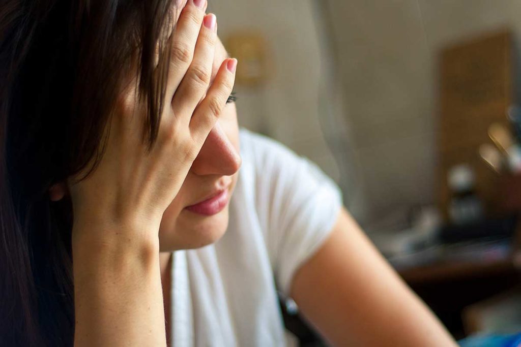 woman sitting in darkened room clutching her head feeling the long-term effects of addiction