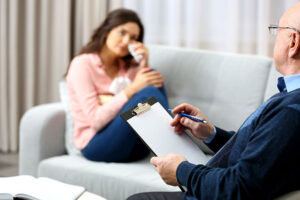 young woman seated on couch in therapist's office undergoing cognitive-behavioral therapy