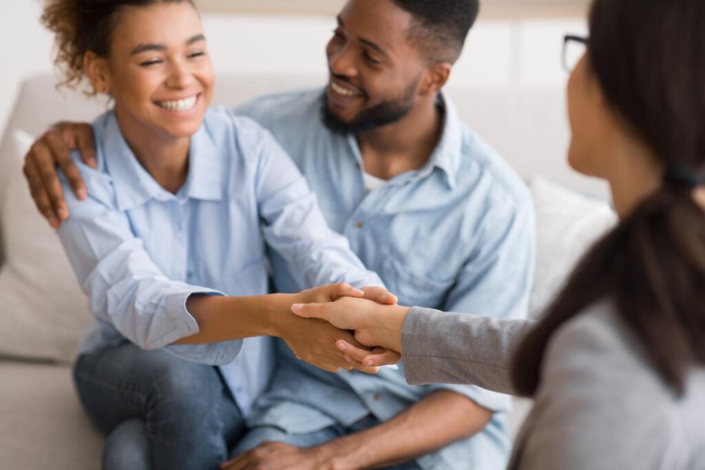 therapist shaking hand of a smiling young man who is seated next to his father as they discuss the benefits of a family program