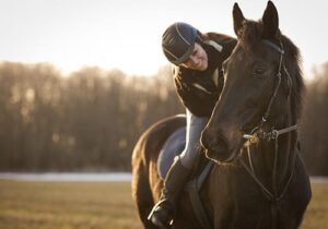 young woman riding horse as she leans down, smiles, and pats the horse's neck as part of an equine therapy program for addiction treatment