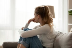 young woman sitting on her couch deep in thought wondering what are the signs of inhalant addiction