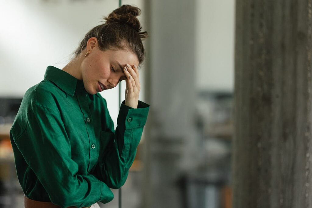 young professionally dressed woman standing in office with her head in one hand with a pained expression experiencing co-occurring disorders and how cocaine can impact your mental health