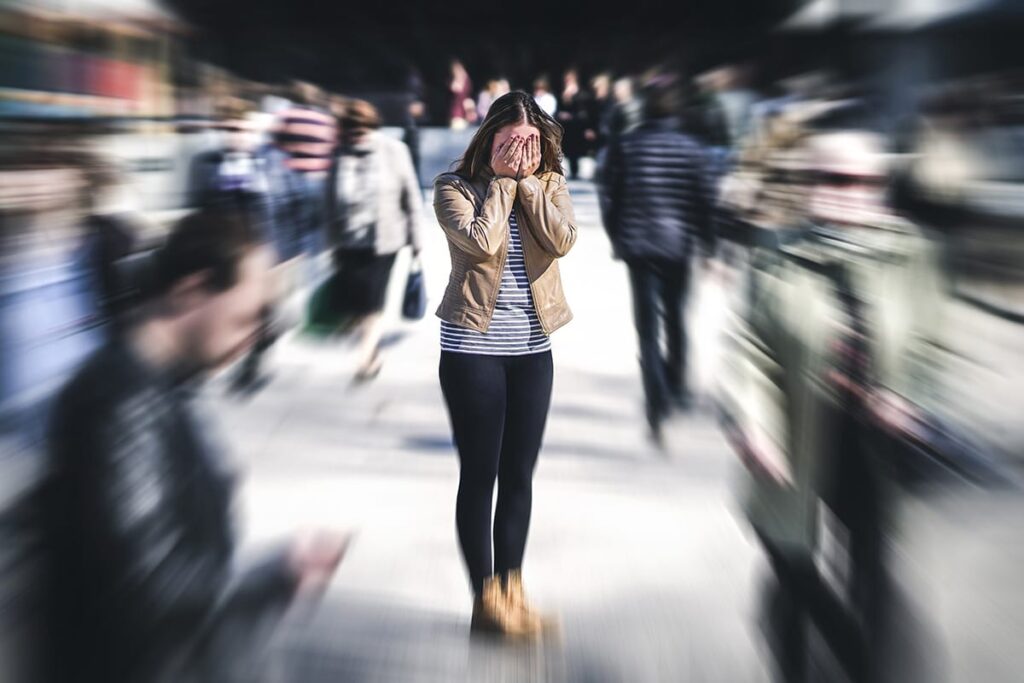 distraught young woman surrounded by blurred images of a crowd as an example of living with social anxiety