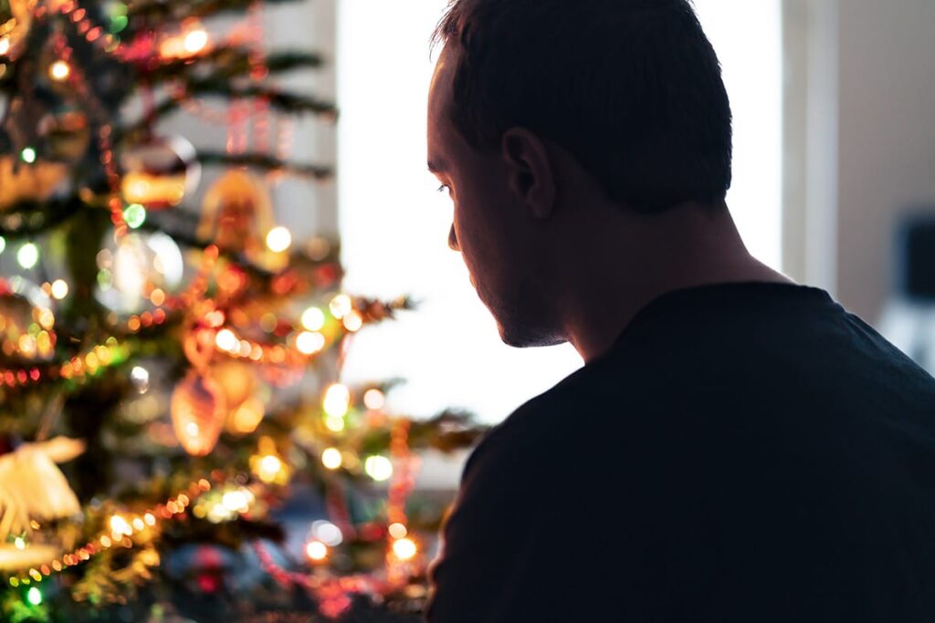 image of a man shrouded in shadow next to a brightly lit Christmas tree symbolizing how managing depression during the holidays can be hard.