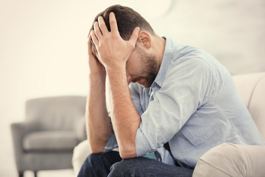 young man seated on couch with head in his hands struggling with the risks of self-medicating