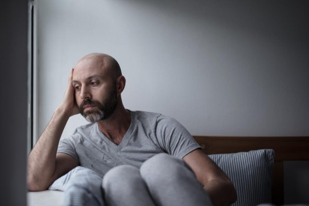 man seated alone on couch in dimly lit room wondering what is a trauma response