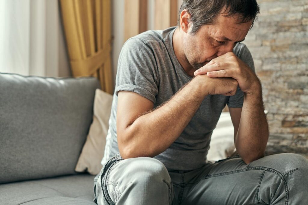 middle aged man seated on couch deep in thought and pondering how does anxiety affect my relationships?