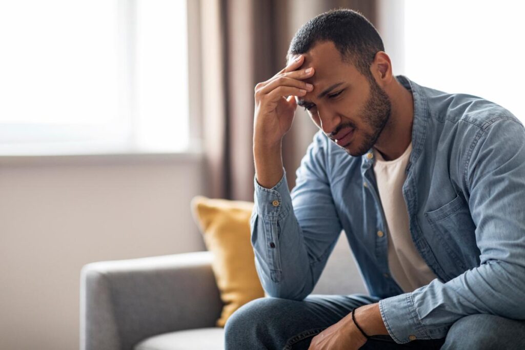 distraught young man seated on couch holding head in pain after discovering what does cocaine feel like?