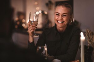 young smiling woman drinking alone at elegant bar and holding up glass of wine as one of many signs of alcoholism in women.