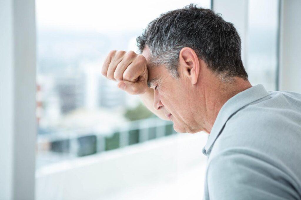 successful middle aged man leaning against window seemingly in pain as he contemplates how cocaine can damage the brain.