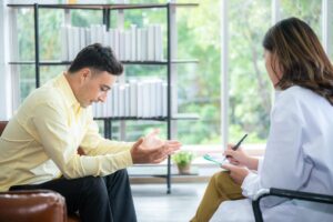 serious young man seated in office and discussing ways of identifying relapse triggers with his addiction treatment specialist.